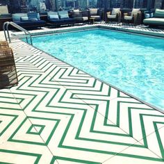 an empty swimming pool with lounge chairs and umbrellas in the background, on top of a high rise building