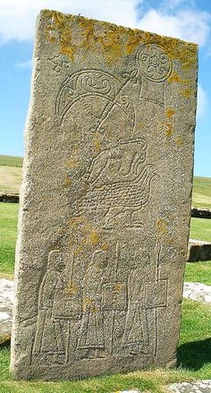 a large stone with carvings on it in the middle of a grassy area next to a field