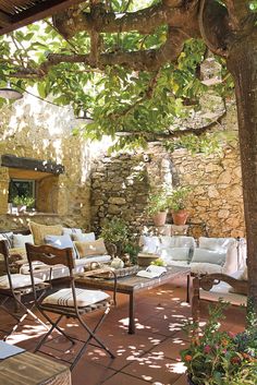 an outdoor living area with chairs, tables and couches under a tree in the shade