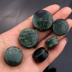 a person holding five green rocks in their left hand and the other one is black with white speckles