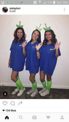 three girls in blue dresses and green socks posing for the camera with their hands up