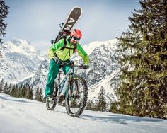 a man riding a bike down a snow covered slope with a snowboard on his back