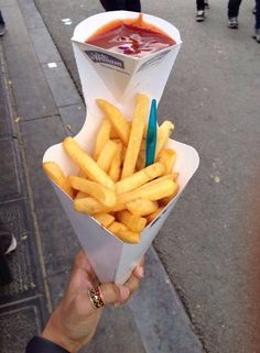 a person holding up a paper container with french fries and ketchup on it