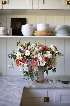 a vase filled with lots of flowers sitting on top of a counter next to plates and bowls