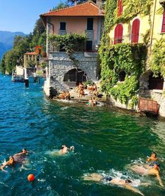 people swimming in the water next to buildings and trees on both sides of the lake