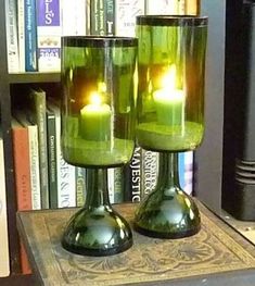 two green candles sitting on top of a table next to bookshelves and a book case