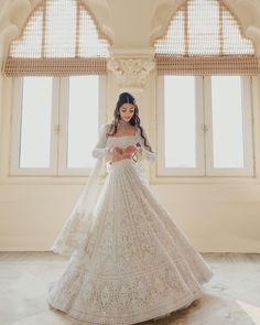 a woman in a white wedding dress standing next to two windows