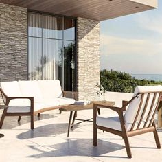 two chairs and a coffee table on a patio near the ocean with a stone wall in the background