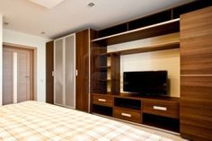 a bed room with a neatly made bed and a flat screen tv on a wooden entertainment center