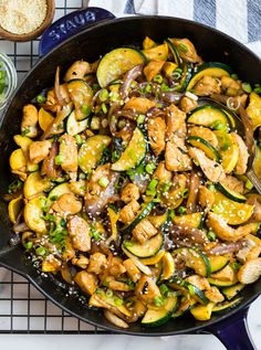 a skillet filled with chicken, zucchini and green onions on top of a table