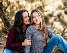 two women sitting next to each other on the ground in front of trees and bushes