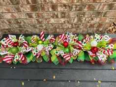 christmas wreaths with green and red bows on a black table next to a brick wall