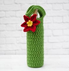 a crocheted green bag with a red flower on it