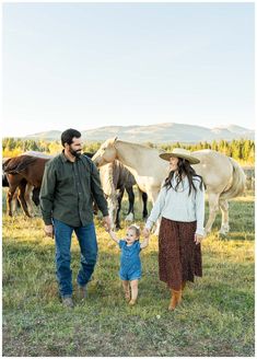 a man and woman holding hands while walking with a small child in front of horses