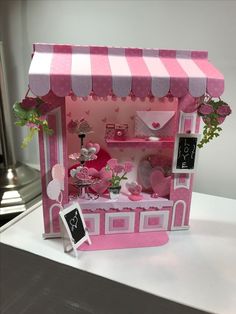 a pink and white doll house with flowers on the table next to it's shelf