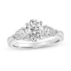 a three stone engagement ring with diamonds on the shoulders and an oval cut diamond in the center