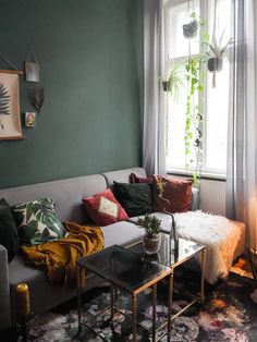 a living room filled with furniture and a plant on the wall next to a window