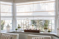 a living room filled with white furniture and windows covered in blinds over the top of them