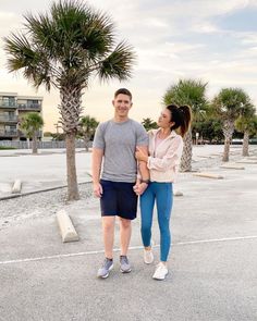 a man standing next to a woman in a parking lot with palm trees behind them