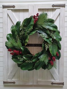 a christmas wreath hanging on the side of a white door with greenery and berries