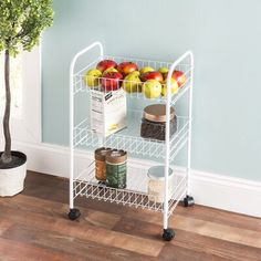 a white wire shelf with apples and other food items on it next to a potted tree