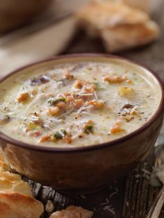 a bowl of soup sitting on top of a wooden table next to some bread pieces