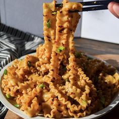 someone is holding up some noodles with chopsticks to eat it on a plate