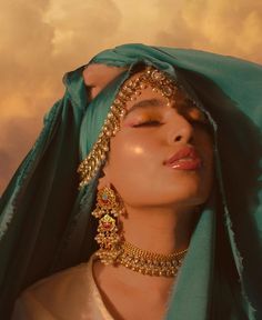 a woman with her eyes closed wearing gold jewelry and a green shawl over her head