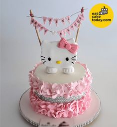 a hello kitty cake is decorated with pink ruffles and bunting on top