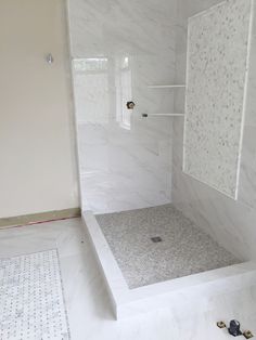 a white bathroom with marble flooring and tile shower stall, built in to the wall