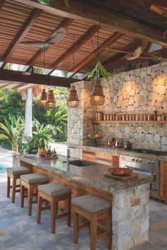 an outdoor kitchen with stone counter tops and stools next to the bar area that's surrounded by greenery