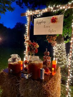 an outdoor display with apples and cider in mason jars on hay bales at night