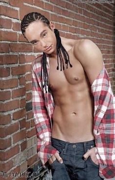 a shirtless man with dreadlocks leaning against a brick wall and looking at the camera