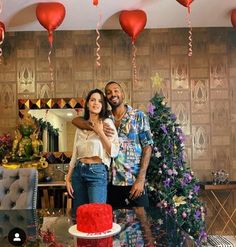 a man and woman standing in front of a cake with red balloons hanging from the ceiling