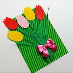 paper flowers are arranged on top of a green mat with pink ribbon and bow around them