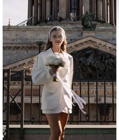 a woman holding a bouquet of flowers in front of a building with statues on it