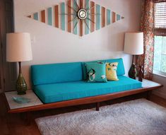 a blue couch sitting in front of a window next to a table with two lamps on it