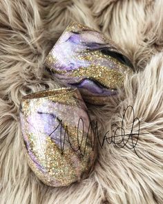 two purple and gold painted rocks sitting on top of a furry surface