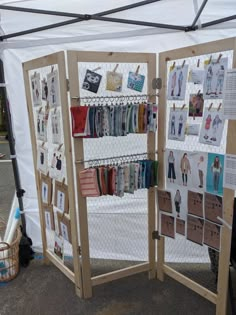 an outdoor display with clothes and handbags hanging on it's sides, in front of a white tent