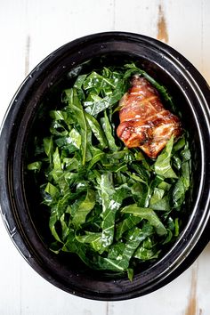 a bowl filled with greens and meat on top of a table