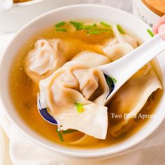 a person holding a spoon in a bowl of soup with dumplings and broth