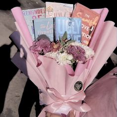 a bouquet of flowers is wrapped in pink paper and sits on the ground next to books