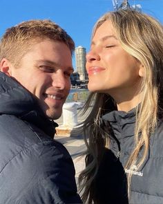 a man and woman standing next to each other in front of a cityscape