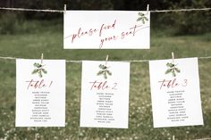 wedding seating signs hanging on a rope in the grass with flowers and leaves painted on them