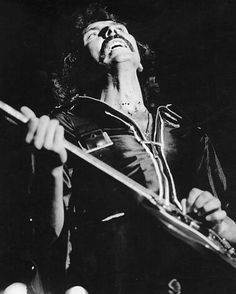 a black and white photo of a man holding a guitar in his right hand while looking up at the sky