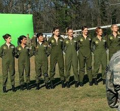 a group of women in green uniforms standing next to each other on grass with trees in the background