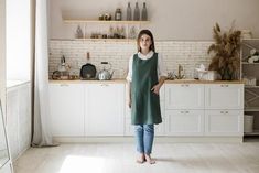 a woman standing in the middle of a kitchen with white cabinets and shelves behind her