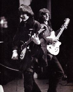 two young men are playing guitars on the street