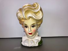 a statue of a woman with blonde hair and pearls on it's head is sitting on a table