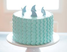 a blue cake with white frosting and two small sharks on top, sitting on a plate